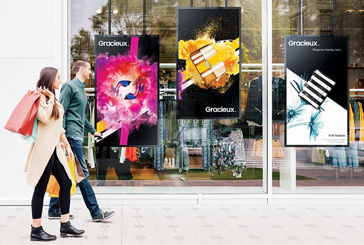 Samsung OM window-facing displays mounted behind a retail storefront window and showing bright promotional content in daylight.